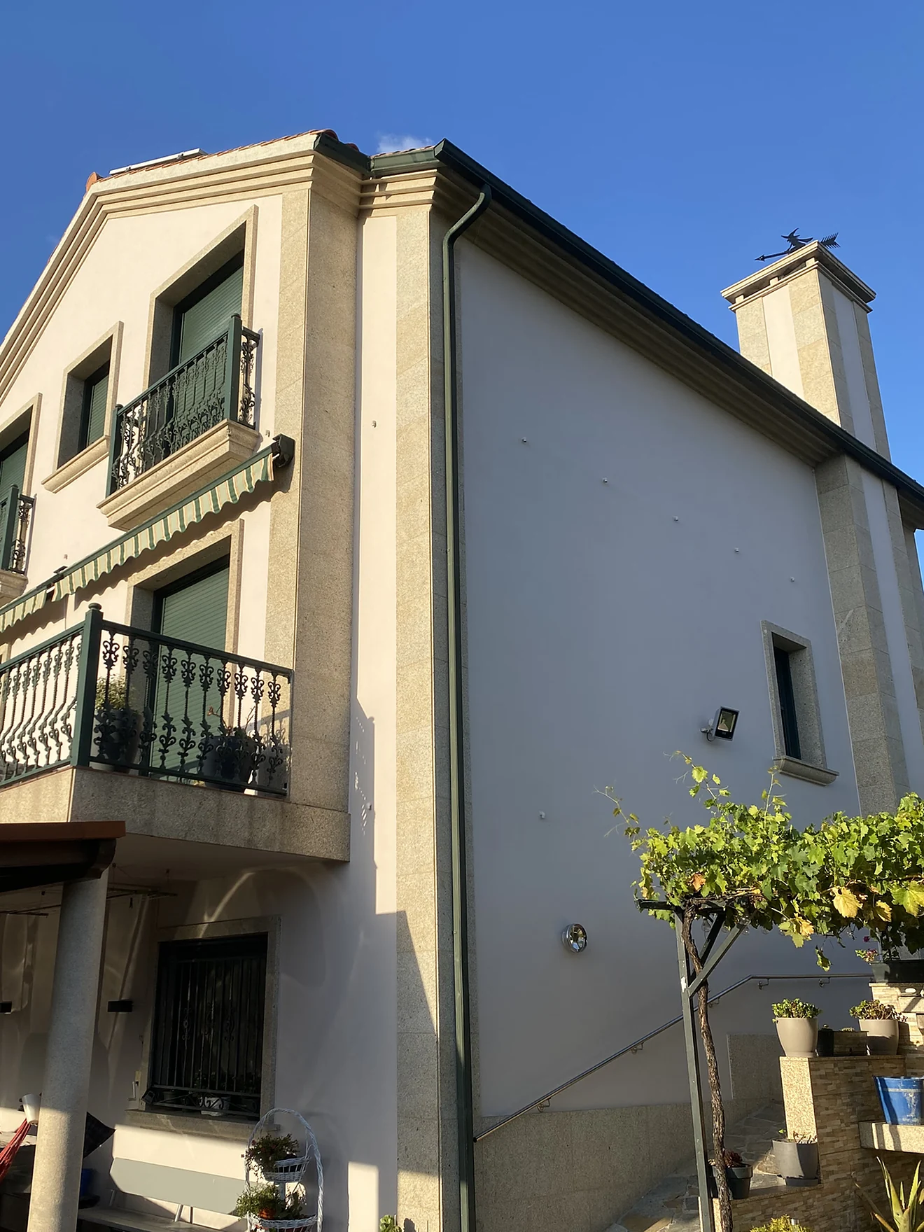 Fachada de vivienda unifamiliar repintada en tono crema, con la piedra de granito limpia, después de la intervención de Luxor